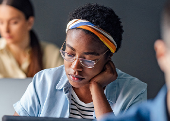 Person with glasses and a colorful headband focusing intently on a laptop in a office setting.